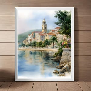 May include: Watercolor painting of a coastal town with a church tower, red-tiled roofs, and palm trees. The artwork depicts buildings along the shoreline, with reflections in the water. The painting is framed in a white border.
