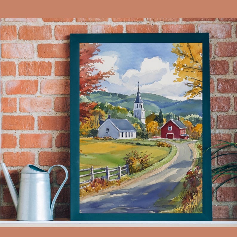 May include: A watercolor painting of a small town with a white church, a red barn, and a winding road. The painting is framed in a dark green frame and is set against a brick wall.