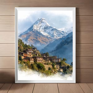 Puede incluir: Una impresión en acuarela enmarcada de un pueblo de montaña. La obra presenta un pico montañoso nevado en el fondo, con un pueblo de edificios de piedra y árboles verdes en primer plano. El cielo es azul suave.