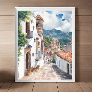 May include: A watercolor painting of a narrow, winding street in a European village. The street is lined with white buildings with terracotta tile roofs. The buildings have balconies and windows, and there are trees and plants growing along the sides of the street. In the distance, there are mountains and a blue sky with white clouds.