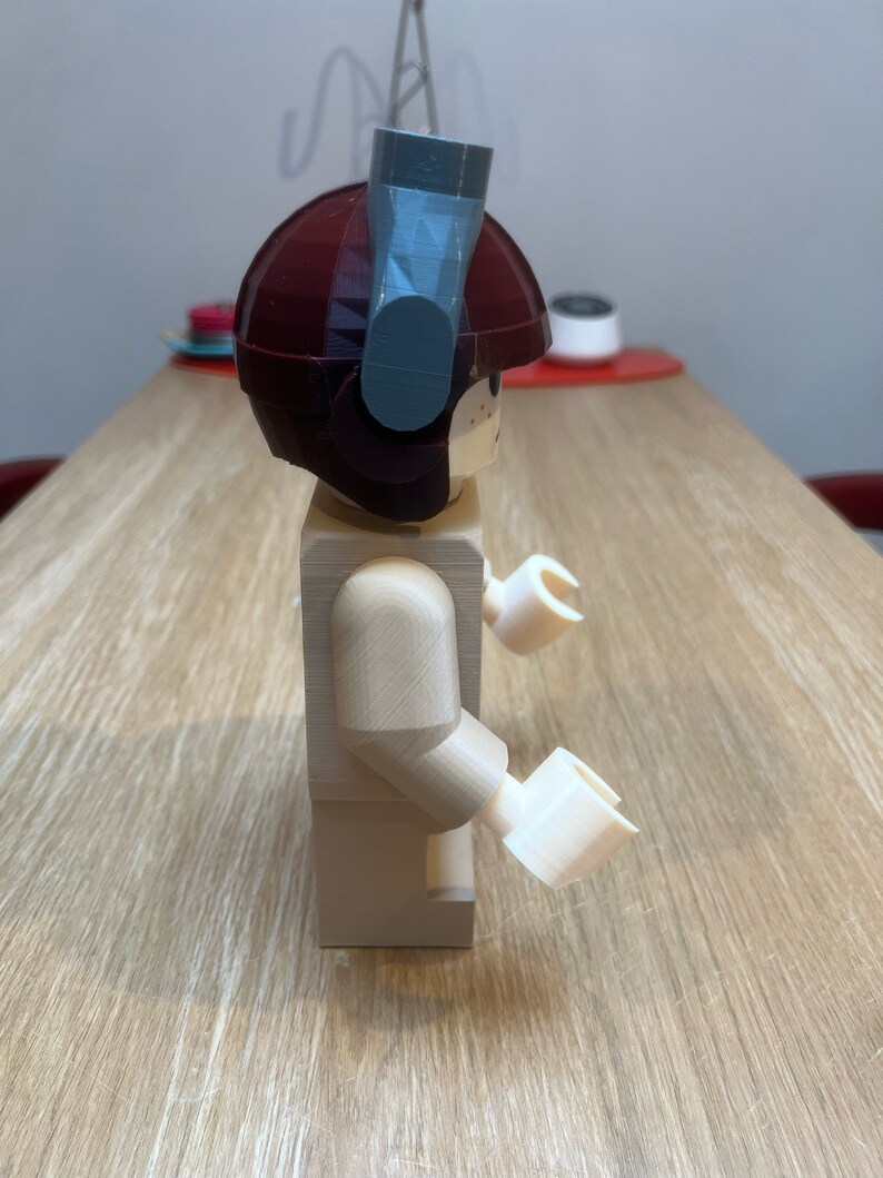Puede incluir: Una minifigura Lego beige con un casco marr&oacute;n y un accesorio gris en la parte superior. La minifigura tiene brazos y manos blancos.