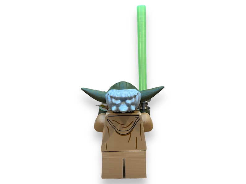 May include: A green and brown Lego minifigure of Yoda from Star Wars holding a green lightsaber. The minifigure is facing away from the camera.