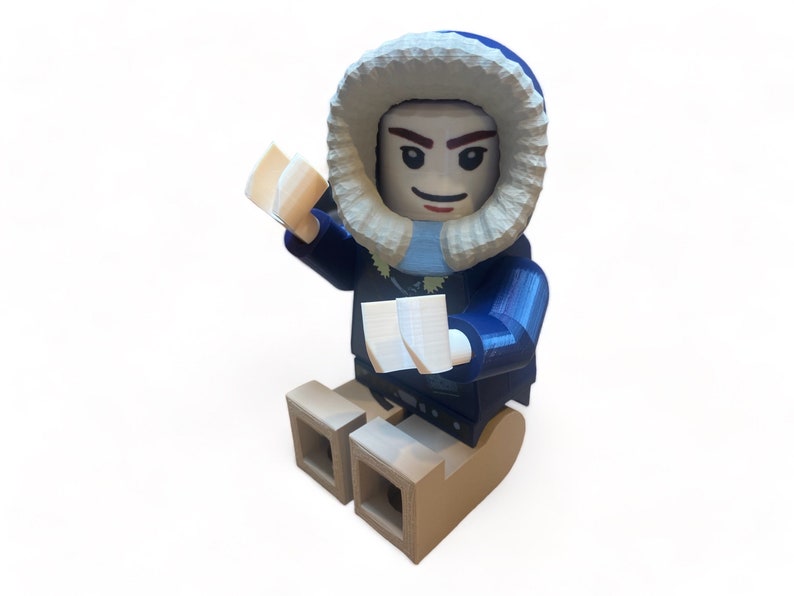 May include: A 3D-printed figurine of a person in a blue parka with a white fur-lined hood. The figure is holding two white objects and is seated on a brown sled-like base. The figure has a smiling expression.