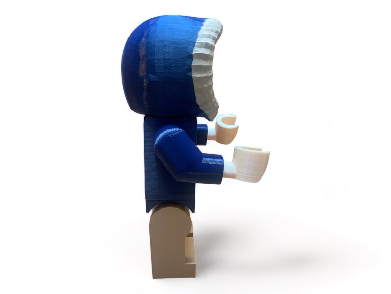 May include: A blue and white Lego-style figure with a hooded parka. The figure has white hands and tan legs. The parka hood is blue with a white trim. The figure is standing on a white surface.
