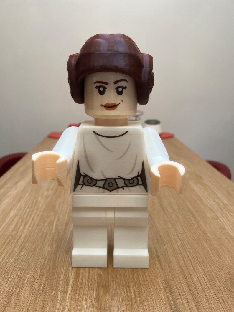 Puede incluir: Una figura de Lego blanca de la princesa Leia de Star Wars. Tiene una peluca marr&oacute;n y un vestido blanco con un cintur&oacute;n negro.