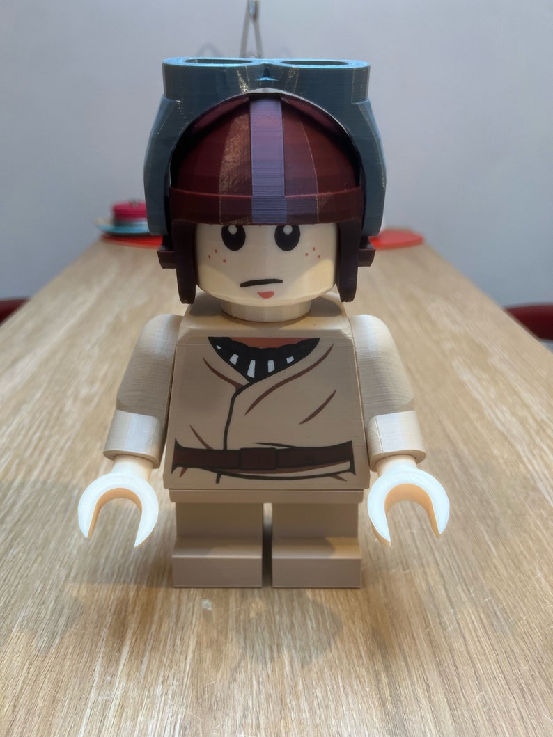 Puede incluir: Una minifigura Lego marr&oacute;n y blanca con un casco azul y marr&oacute;n. La minifigura lleva una t&uacute;nica marr&oacute;n y blanca.