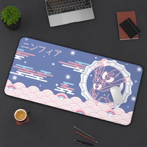Op de afbeelding: Blauwe rechthoekige muismat met een Japans geïnspireerd ontwerp. Het heeft een stripfiguur in een cirkelvormig frame, Japanse tekst en wolken- en golfpatronen in roze, wit en blauw. Een computermuis rust op de mat.