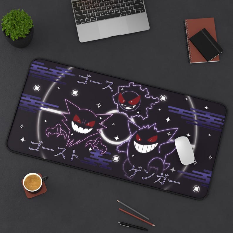 May include: Black rectangular desk mat with a purple and white design featuring three cartoon ghost characters and Japanese text. A white computer mouse is on the mat. The mat is on a black desk.