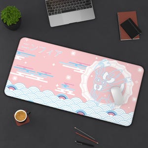 Pode incluir: Tapete de rato retangular rosa com um design de personagem de desenho animado. O tapete de rato apresenta um fundo rosa claro com texto japonês, desenhos de nuvens azuis e brancas e um rato branco. Uma pequena planta, um laptop e uma chávena de café também são visíveis.