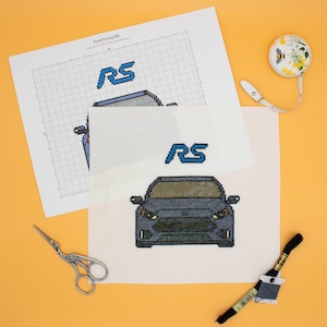 Puede incluir: Un patrón de punto de cruz para un coche Ford Focus RS. El patrón incluye un logotipo RS azul y un coche gris con detalles negros. El patrón está impreso en papel blanco con una cuadrícula.