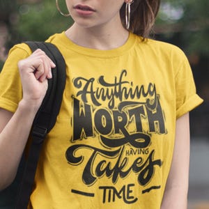 Puede incluir: Camiseta amarilla con texto negro que dice "Anything worth having takes time".