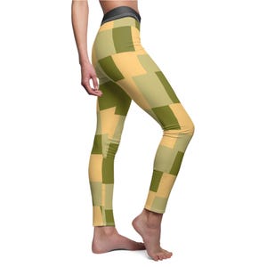 May include: High-waisted leggings with a geometric pattern of olive green and tan squares. The leggings have a black waistband and are made of a stretchy material. The design is repeated throughout the leggings.