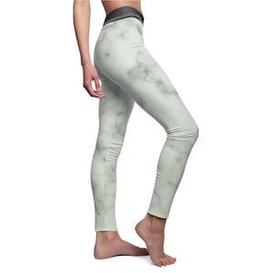 Op de afbeelding: Lichtgrijze legging met een marmerpatroon. De legging heeft een zwarte tailleband en een nauwsluitend ontwerp. Het marmerpatroon heeft subtiele grijze aderen tegen een lichtgrijze achtergrond. De legging is gemaakt van een zacht, rekbaar materiaal.