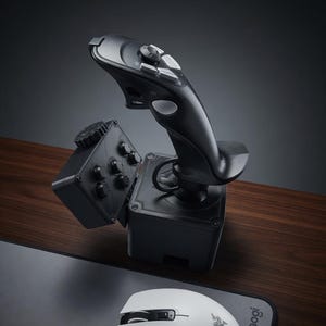 May include: A black joystick with multiple buttons and a base, and a white computer mouse. The joystick is on a wooden surface, with the mouse and a mousepad in the foreground. The mousepad has the word "Raogi" printed on it.