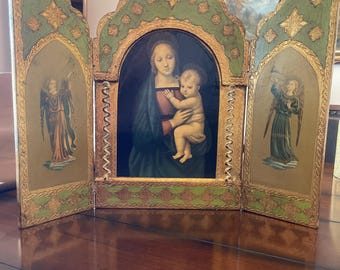 Pode incluir: Um tríptico de madeira de três painéis com acabamento pintado em dourado e verde. O painel central apresenta uma pintura da Virgem Maria segurando o menino Jesus. Os painéis laterais apresentam pinturas de anjos.