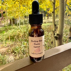 May include: A brown glass bottle with a black dropper cap. The label reads "Shooting Star Flower Essence" and "Forest Moon Medicine". The bottle is set against a backdrop of yellow foliage and trees.