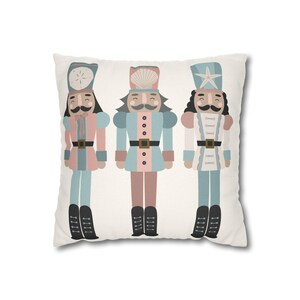 Può includere: Cuscino quadrato decorativo con tre illustrazioni di soldati schiaccianoci stravaganti. Ogni schiaccianoci è vestito con colori pastello con stivali neri e una cintura dorata. Gli schiaccianoci hanno diversi disegni di cappelli.