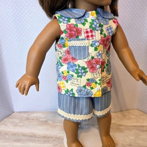 May include: Doll clothing set featuring a floral print top with a blue collar and matching striped shorts. The top has a pocket and button closure. The shorts have a lace trim. The outfit is designed for a doll.