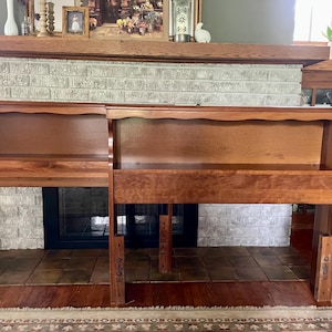 May include: Two wooden headboards with a warm, reddish-brown finish. Each headboard has a shelf and a lower section, with decorative details along the top edge. The headboards are positioned in front of a fireplace.
