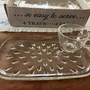 Puede incluir: Un juego de bandeja y taza para aperitivos de vidrio transparente con un patrón de gotas texturizado. La bandeja tiene asas festoneadas y una hendidura circular para la taza. La caja original incluye el texto ...so easy to serve... 4 TRAYS... 4 CUPS.