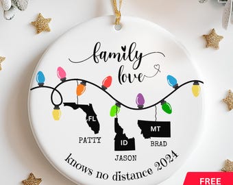 May include: White ceramic Christmas ornament with a string of colorful lights, the states of Florida, Idaho, and Montana, and the text "family love knows no distance 2024".