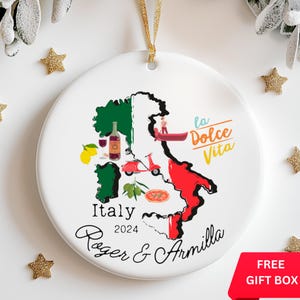 May include: White ceramic Christmas ornament with a map of Italy, featuring iconic symbols like a gondola, a Vespa scooter, a pizza, and olives. The text "Italy 2024 Roger & Armilla" and "la Dolce Vita" are printed on the ornament.