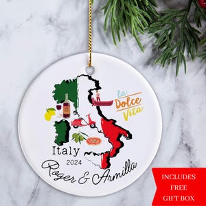 May include: A white ceramic ornament with a map of Italy, featuring a red and green color scheme. The ornament includes the text "Italy 2024 Roger & Armilla" and "la Dolce Vita".