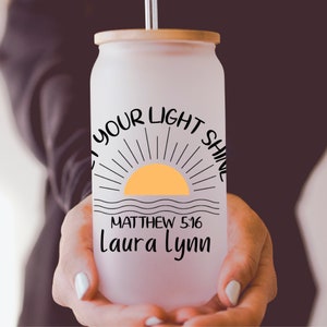 May include: White frosted glass tumbler with a bamboo lid and a straw. The tumbler has a black graphic of a sun with rays and the text "Let your light shine" above it. Below the sun is the text "Matthew 5:16" and "Laura Lynn".