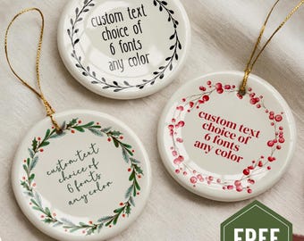 Puede incluir: Tres adornos redondos de cerámica blanca con cordones dorados. Cada uno presenta un diseño de corona decorativa y el texto: custom text choice of 6 fonts any color. Una corona es negra, otra es verde con bayas rojas y otra es de bayas rojas.