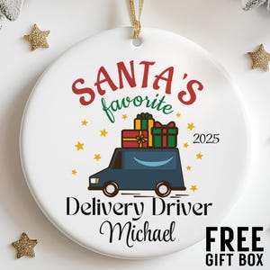 May include: White ceramic Christmas ornament with the text "Santa's Favorite Delivery Driver Michael 2025". The ornament features a blue delivery truck carrying gifts, surrounded by yellow stars. Gold star-shaped decorations are scattered around the ornament.