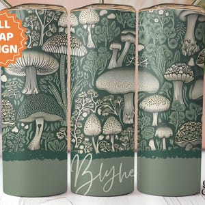 Puede incluir: Un vaso verde con un dise&ntilde;o envolvente completo que presenta una ilustraci&oacute;n bot&aacute;nica de varias setas y follaje. El dise&ntilde;o incluye el nombre "Blythe" en cursiva. El vaso tiene una base verde oscuro.