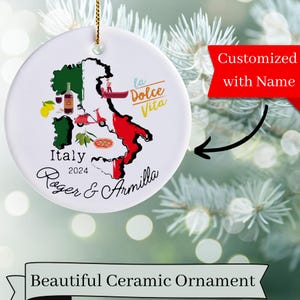 May include: A white ceramic Christmas ornament with a map of Italy, featuring a red, white, and green color scheme. The ornament includes the text "Italy 2024" and "Roger & Armilla". The ornament also features a gondola, a scooter, a pizza, and a bottle of wine.