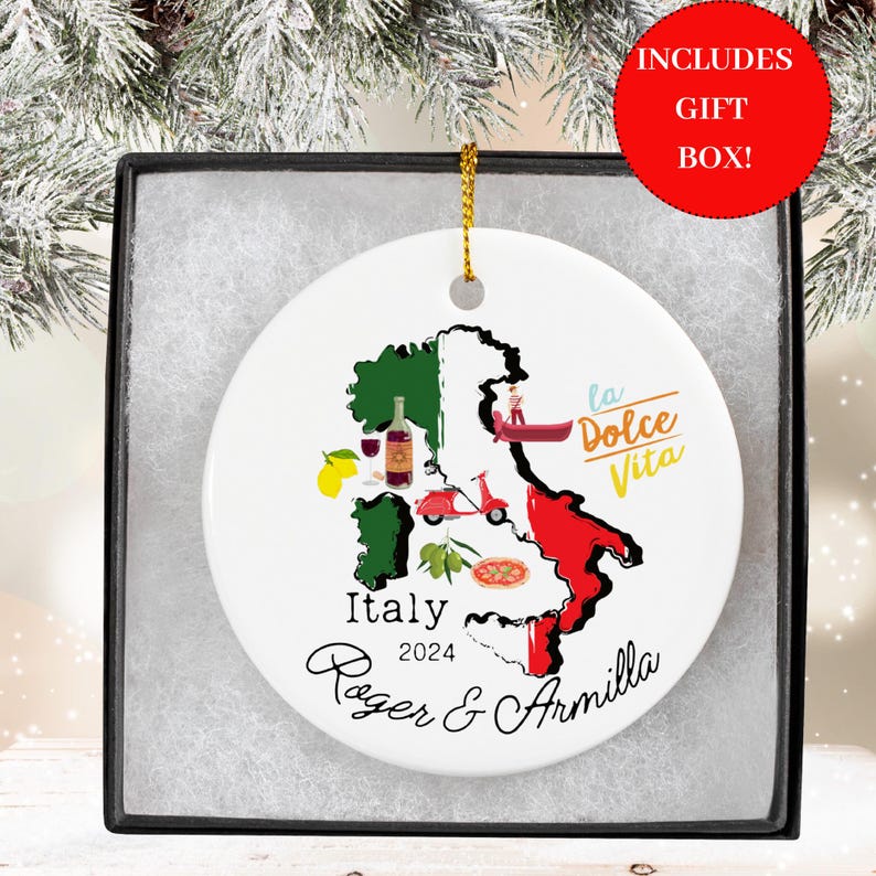 May include: White ceramic Christmas ornament with a map of Italy, featuring iconic symbols like a gondola, a Vespa scooter, lemons, olives, and a pizza. The text "Italy 2024 Roger & Armilla" and "La Dolce Vita" are printed on the ornament.
