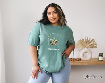 May include: A light green t-shirt with a graphic of a stack of books and the text "expanding my mind, reading is thriving, bookworm".