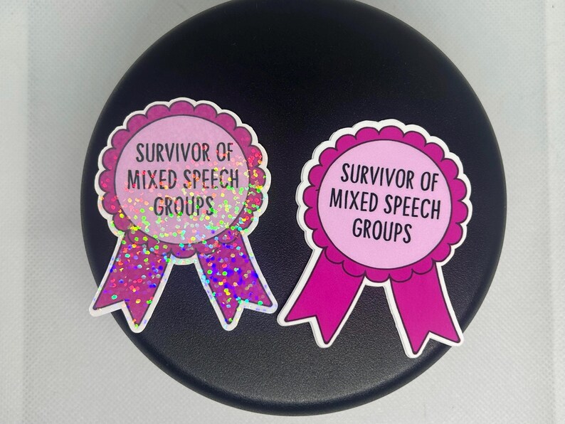 K&ouml;nnte beinhalten: Zwei rosa und lila Aufkleber mit dem Text "Survivor of Mixed Speech Groups". Die Aufkleber sind wie Schleifen mit gewellten R&auml;ndern geformt. Ein Aufkleber hat einen glitzernden, holografischen Effekt.