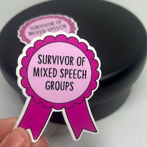 K&ouml;nnte beinhalten: Ein rosa-wei&szlig;er Aufkleber mit dem Text "Survivor of Mixed Speech Groups" in einem kreisf&ouml;rmigen Design mit einem Band. Ein weiterer Aufkleber ist im Hintergrund sichtbar. Der Aufkleber wird von einer Hand gehalten.