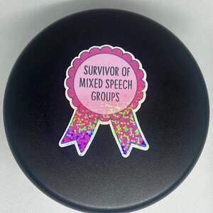 K&ouml;nnte beinhalten: Runder Aufkleber mit dem Text "Survivor of Mixed Speech Groups" in einem rosa-wei&szlig;en, gewellten Design. Der Aufkleber hat ein rosa-violettes Band mit Glitzerakzenten auf schwarzem Hintergrund.