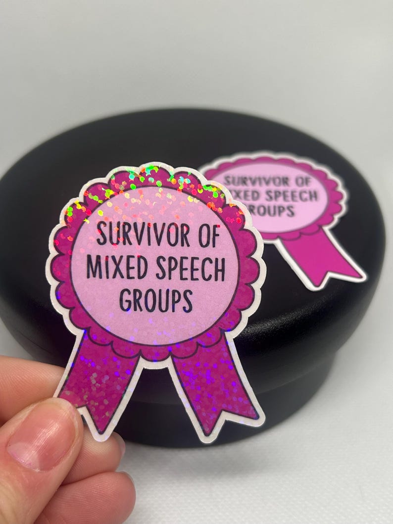 K&ouml;nnte beinhalten: Zwei rosa und glitzernde Aufkleber mit dem Text "Survivor of Mixed Speech Groups" in schwarzer Schrift. Die Aufkleber sind wie Schleifen geformt, mit einem gewellten Rand und einem rosa Band unten.