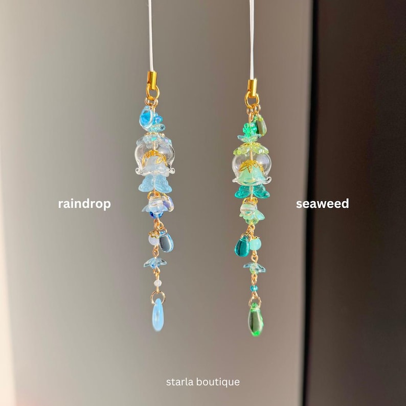 Op de afbeelding: Twee kralenhangers, &eacute;&eacute;n blauw en &eacute;&eacute;n groen, met goudkleurige accenten. De blauwe hanger is gelabeld met "raindrop" en de groene hanger met "seaweed". De hangers hebben een verscheidenheid aan kralen en vormen, waaronder bloem- en druppelvormige ontwerpen. De tekst "starla boutique" staat onderaan.