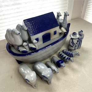 May include: A ceramic Noah's Ark set with a blue and white color scheme. The ark features a blue roof and is filled with pairs of animals, including elephants, giraffes, and zebras. A man and woman figurine are also included.