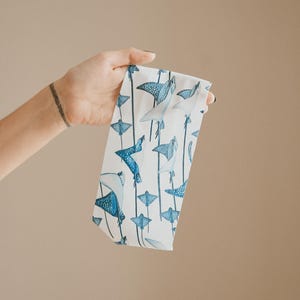May include: A white fabric headband featuring a repeating pattern of blue spotted stingrays and manta rays. The marine life illustrations are rendered in shades of blue and white, arranged in a vertical orientation across the surface of the band.