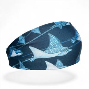May include: A dark blue headband patterned with light blue manta rays. The manta rays have white bellies and are spread across the fabric. The headband is designed to be worn around the head.