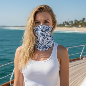 May include: A white sleeveless top and a blue and white neck gaiter featuring a repeating pattern of various shark silhouettes. The fabric covering the lower face and neck displays multiple shark shapes in different sizes and orientations.