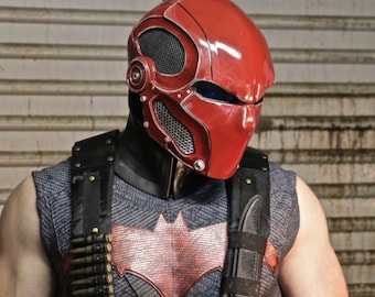 Könnte beinhalten: Ein rot-schwarzes Superhelden-Kostüm mit einem roten Helm mit detailliertem Design. Das Kostüm beinhaltet eine schwarze Weste mit einem roten Fledermaus-Symbol und einen schwarzen Gurt mit einem Messer.