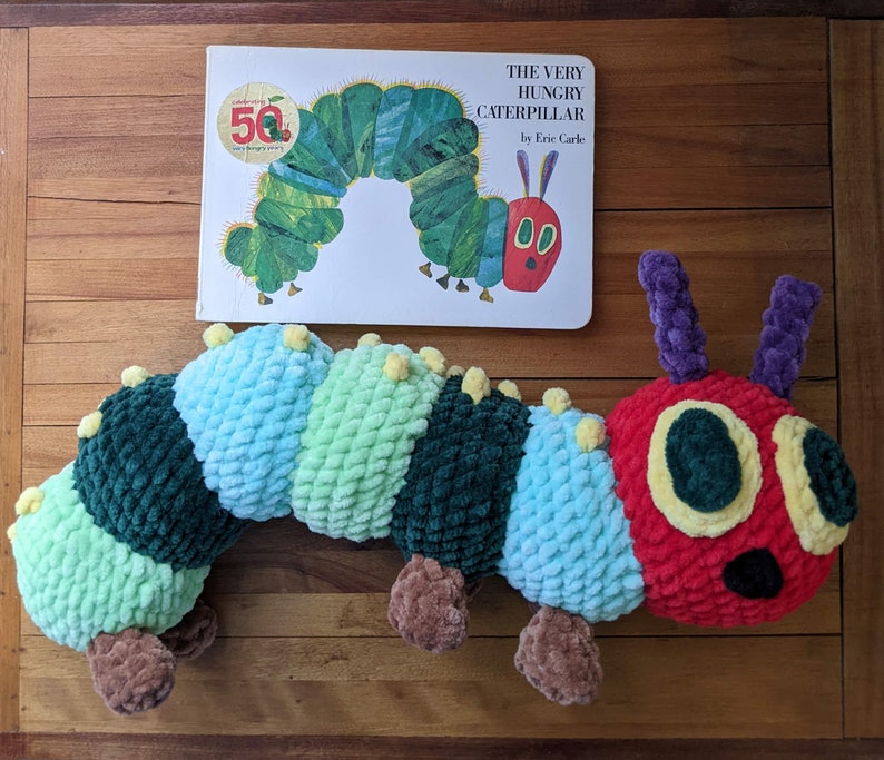 May include: A green and red plush caterpillar toy with a book titled "The Very Hungry Caterpillar" by Eric Carle. The book is celebrating its 50th anniversary.