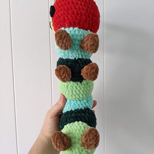 May include: A crocheted caterpillar toy with a red head, green and black body segments, and brown legs.