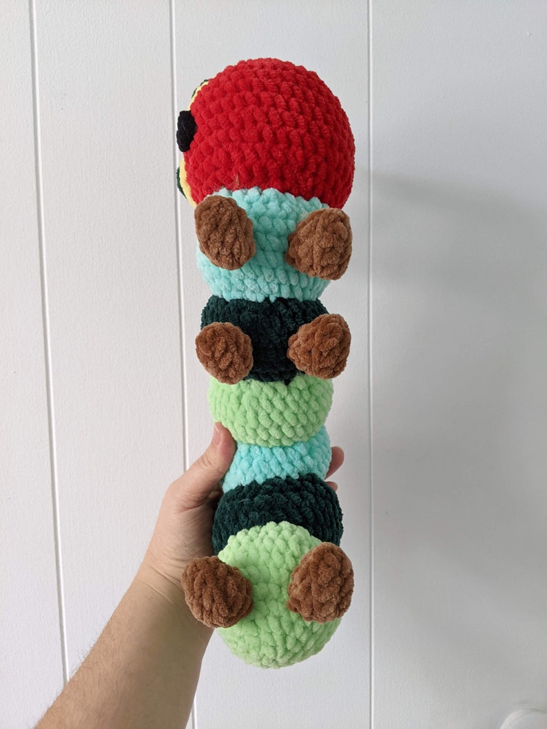 May include: A crocheted caterpillar toy with a red head, green and black body segments, and brown legs.