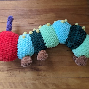 May include: A crocheted caterpillar toy with a red head, green, blue, and light green segments, and brown feet.