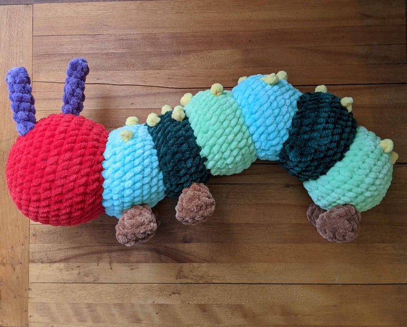 May include: A crocheted caterpillar toy with a red head, green, blue, and light green segments, and brown feet.