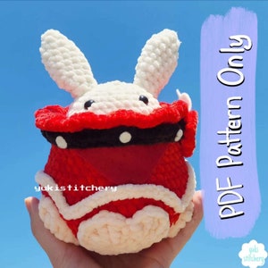 Puede incluir: Patrón de amigurumi de crochet para un conejito rojo y blanco que lleva un disfraz rojo y negro. El patrón está disponible solo como descarga PDF. El texto "PDF Pattern Only" está escrito en morado sobre un fondo azul claro.